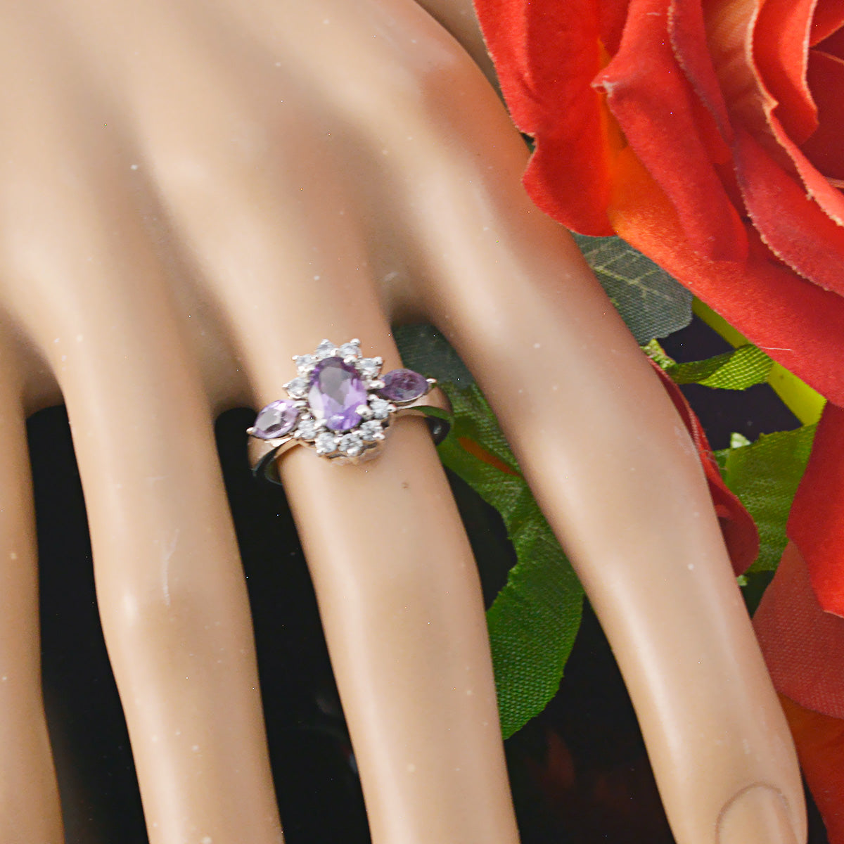 Lily purple gemstone trilogy ring with oval center stone and surrounding smaller stones on hand