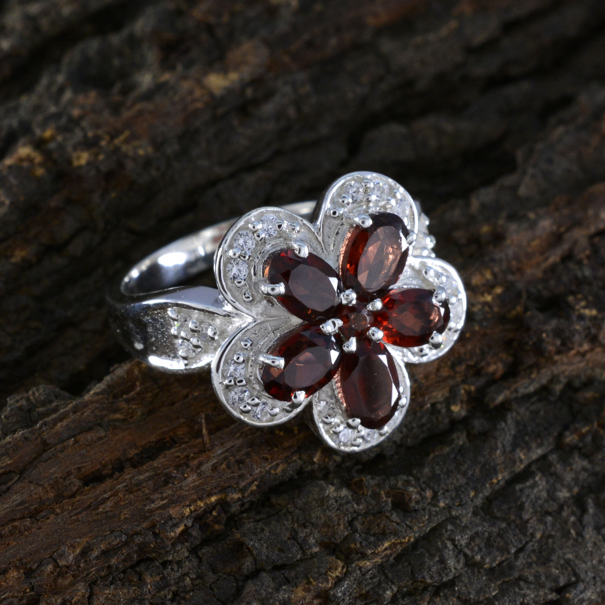 Isla red floral gemstone ring with silver band and red petals on textured wood background