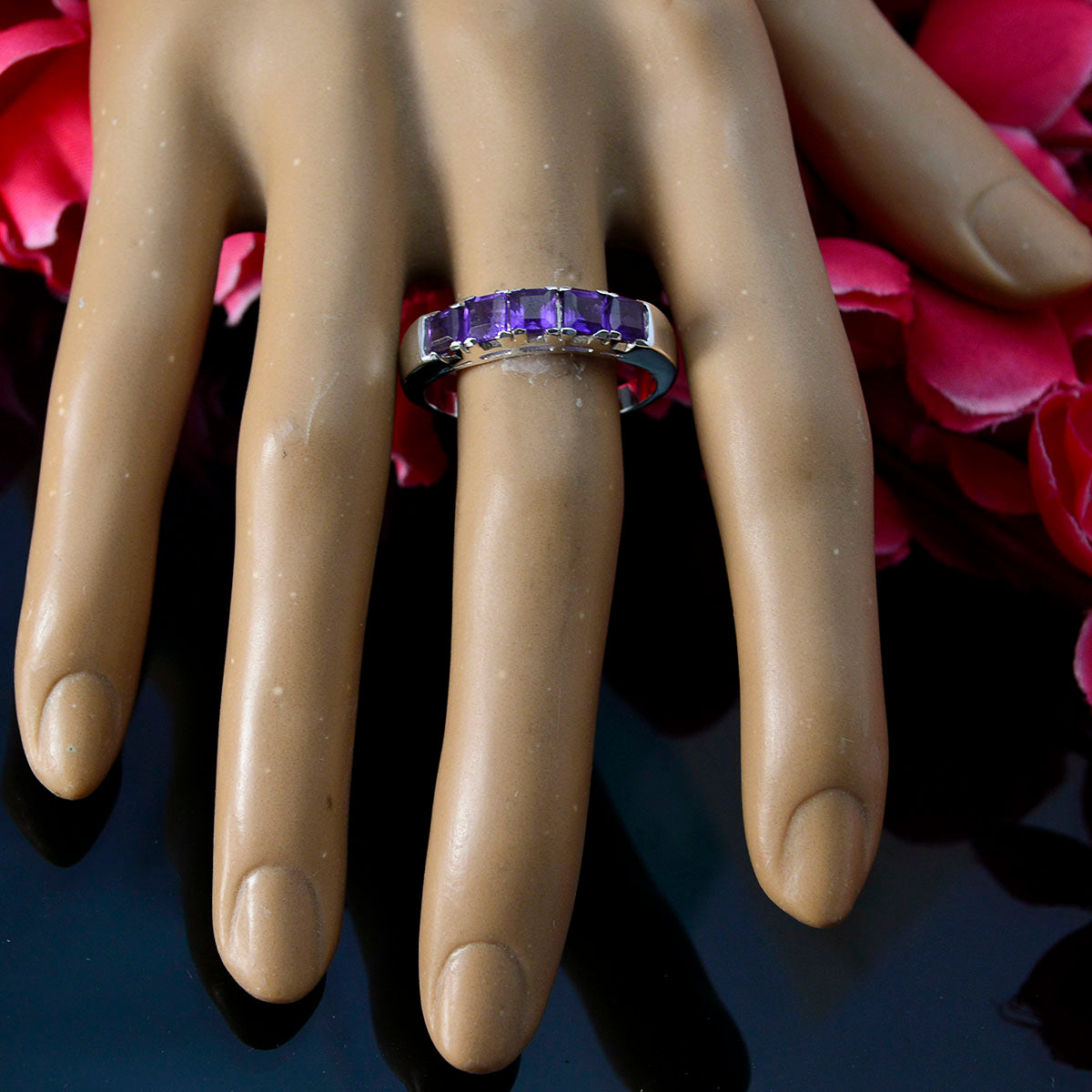 Dayana trendy purple gemstone ring channel set on silver band shown on mannequin hand with pink petals