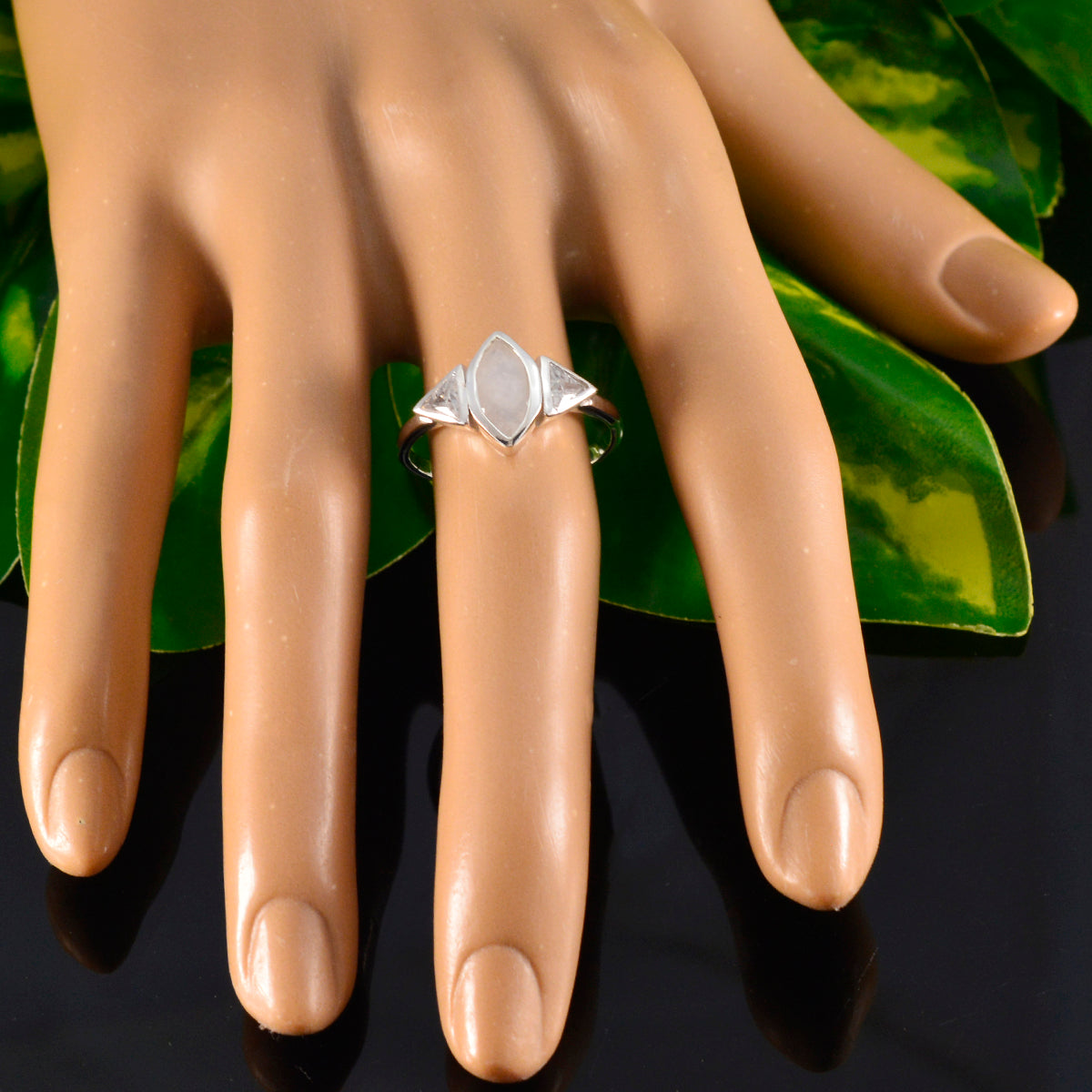 Lucy white trilogy ring with three white stones on a display hand over black and green background