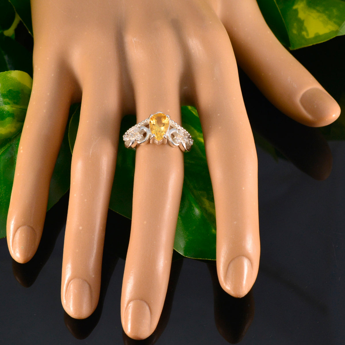Olivia yellow gemstone halo ring on display hand with green leaves background