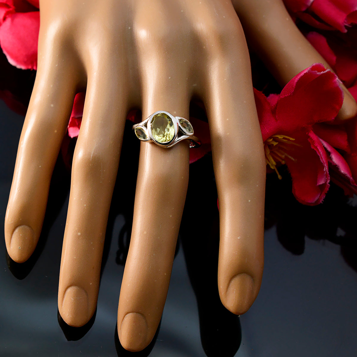 Yellow gemstone trilogy ring by Fernanda on hand with red flowers background