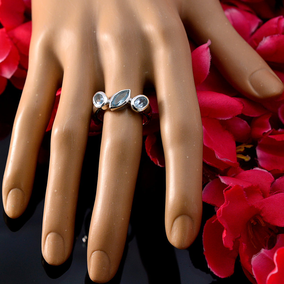 Laura artisan blue gemstone ring with three blue stones on display hand with red flowers background