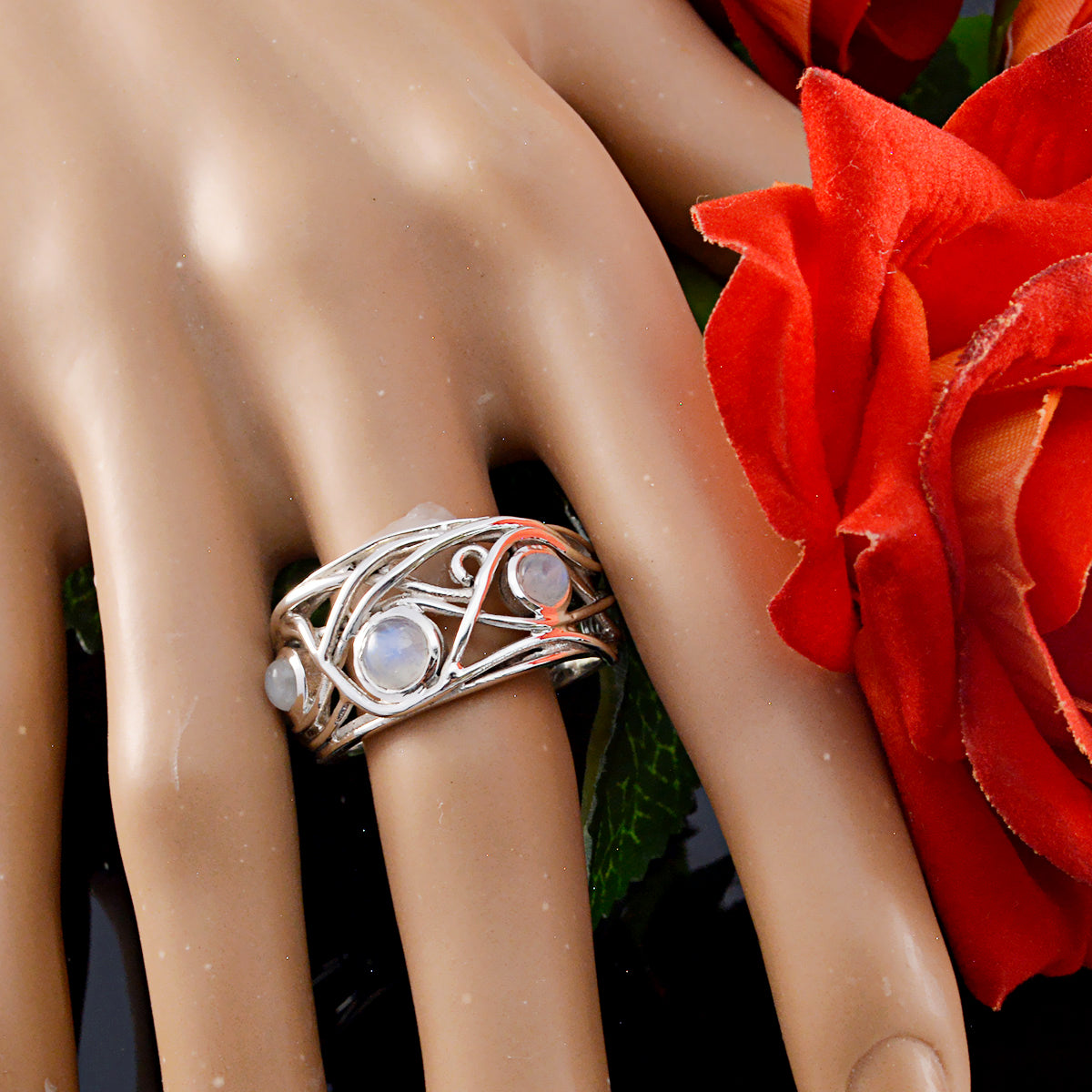 Laura white trilogy ring with intricate silver design and three round gemstones displayed on a hand next to a red flower