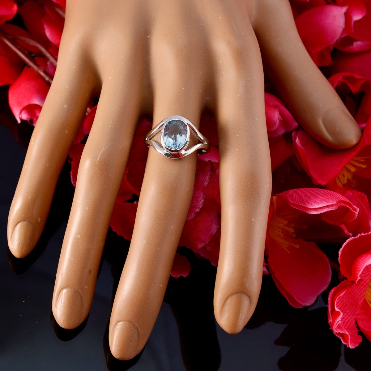 Nari blue solitaire ring for women with oval aquamarine gemstone set in silver ring on mannequin hand over red petals