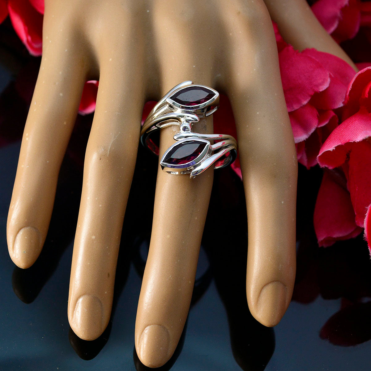 Emma contemporary red gemstone ring with silver band on display hand with red flowers background