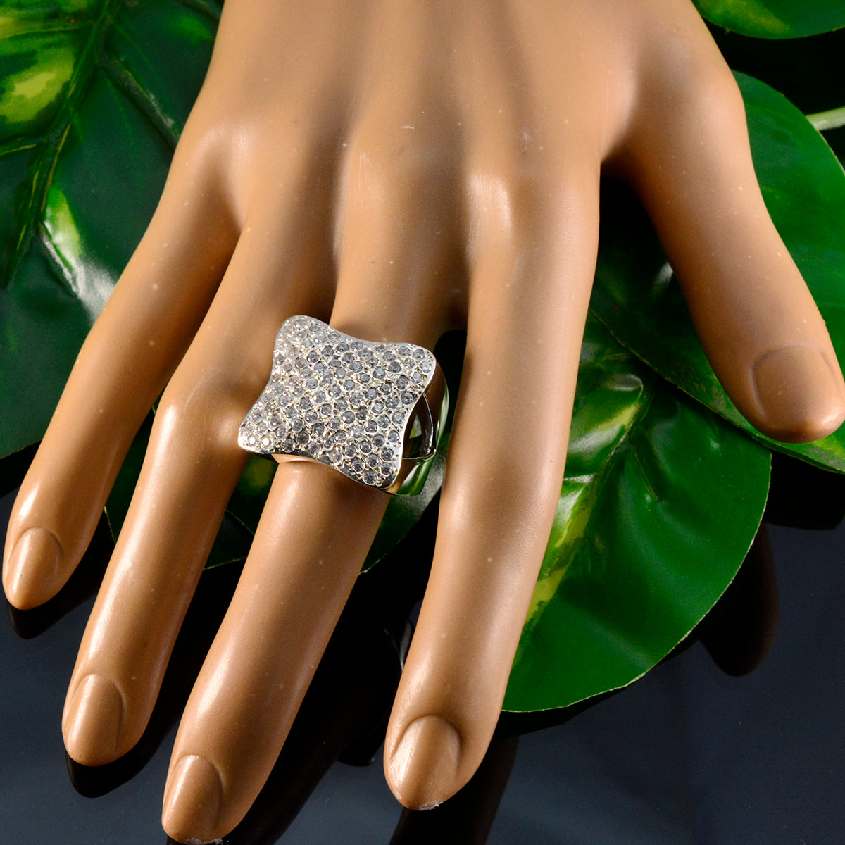 Zoey heritage white ring with intricate design displayed on a mannequin hand among green leaves